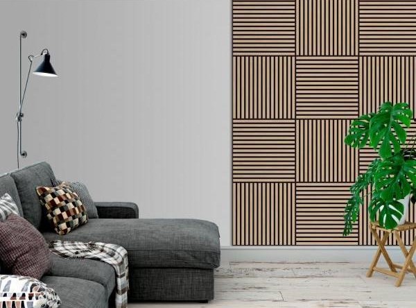A modern living room with a gray modular sofa with decorative pillows, a floor lamp, and a large plant with leaves in a woven basket next to it. The wall has a distinctive design with vertical wooden slats arranged in squares.