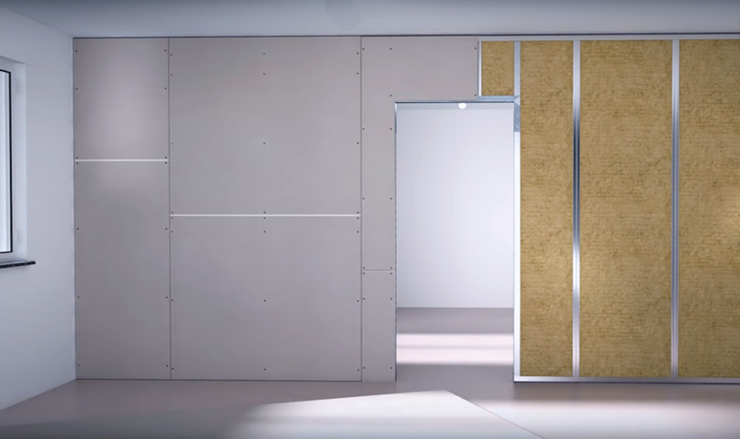 A room with unfinished walls, plasterboard, and a section of wooden wainscoting, with a door on the right.