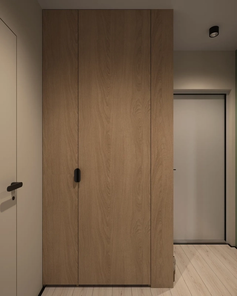 A hallway with wooden paneling, featuring a closed cabinet door and a white door in the background. The flooring is light-colored wood, and there is minimal lighting above.