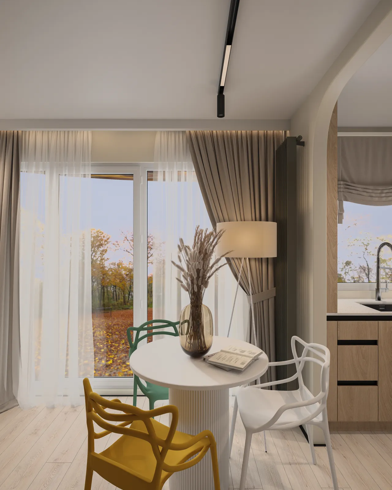 A cozy interior featuring a round white table surrounded by colorful chairs, with a large window allowing natural light to flood the space. There are decorative elements like a vase with dried flowers and soft curtains. The kitchen area can be seen in the background.