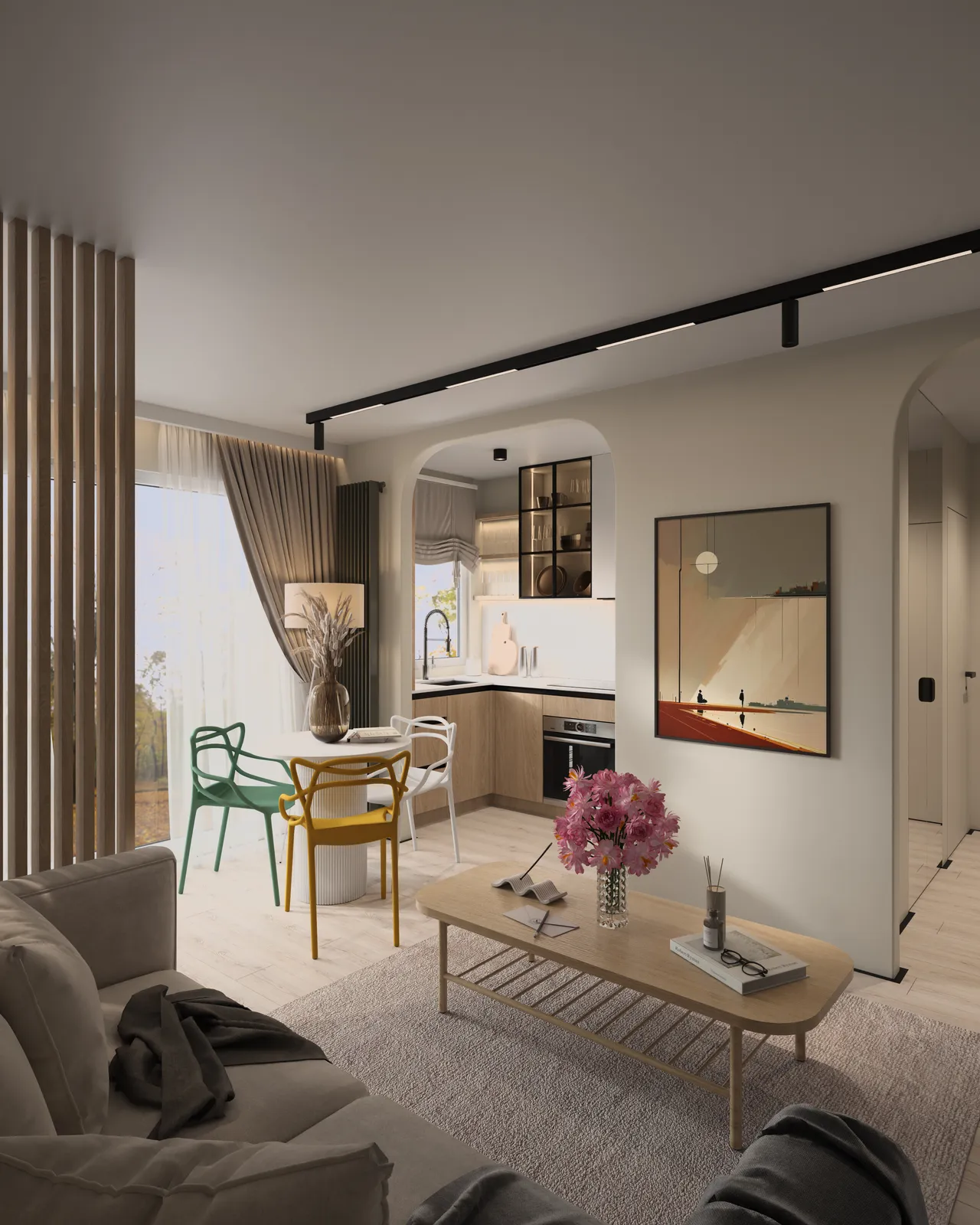 A modern living space featuring a dining area with a round table and colorful chairs, a small kitchen visible in the background, and large windows with natural light illuminating the room. Decorative touches include art on the walls and floral arrangements on the table.