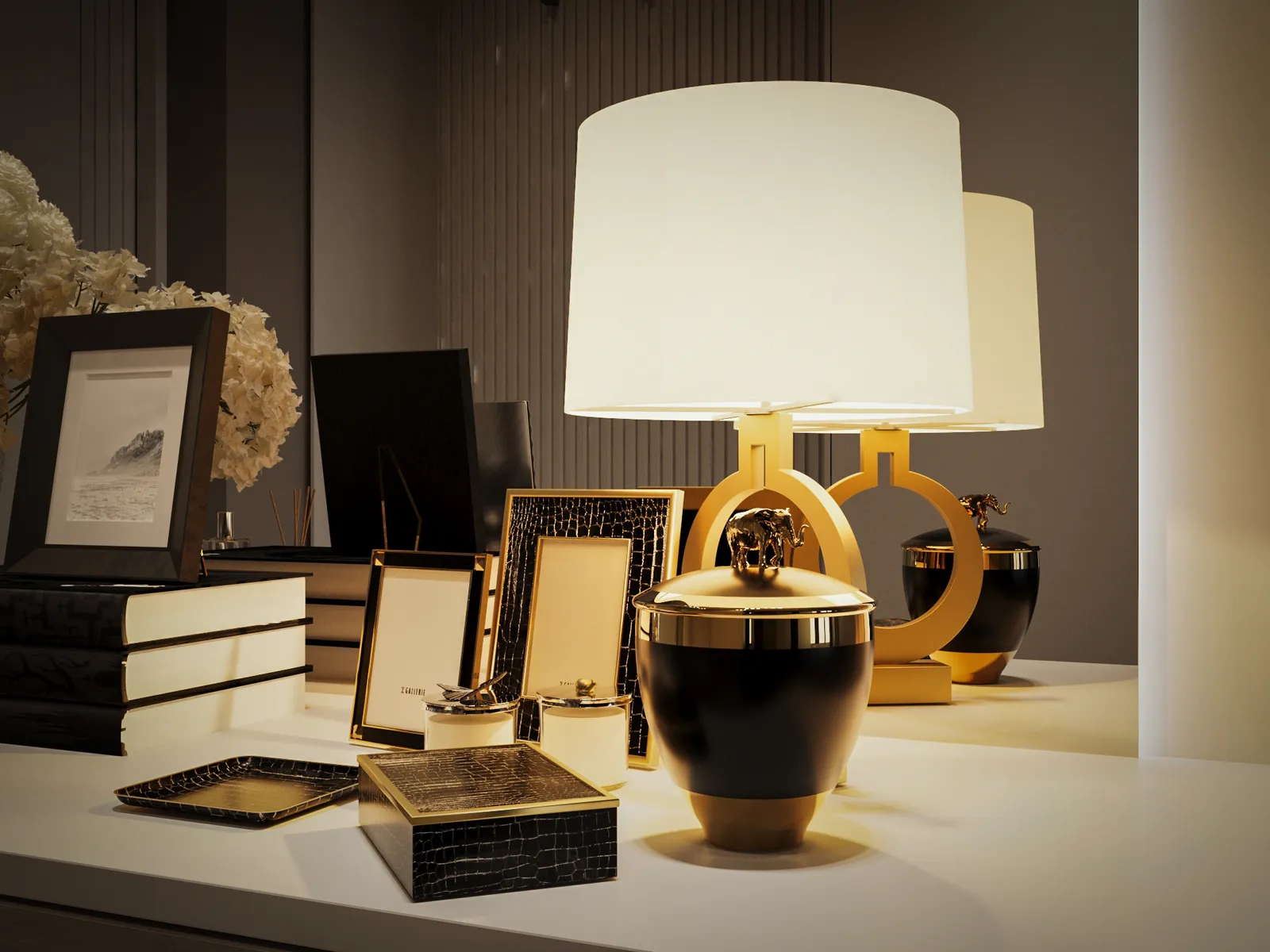 A dark and luxurious tablescape featuring a large white drum lamp, black and gold decorative boxes, several picture frames, and stacked books with white pages.