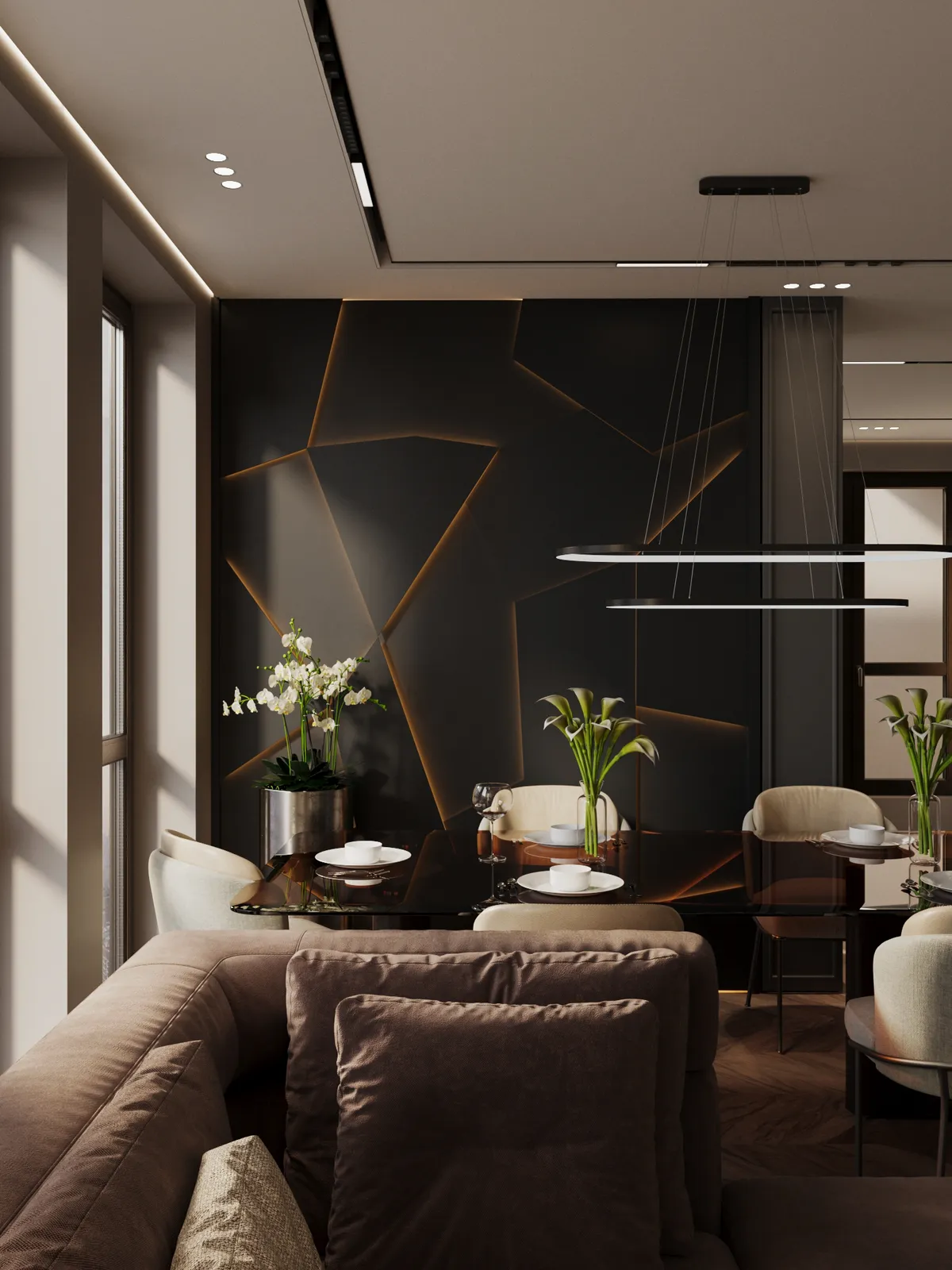A modern living and dining area features a brown sectional sofa, a dark geometric accent wall with amber backlighting, and contemporary hanging light fixtures illuminating a glass dining table set for six.