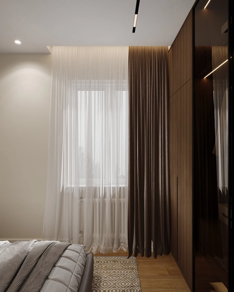 A modern bedroom featuring a window with sheer and dark curtains, a patterned rug, and a bed with a textured duvet.