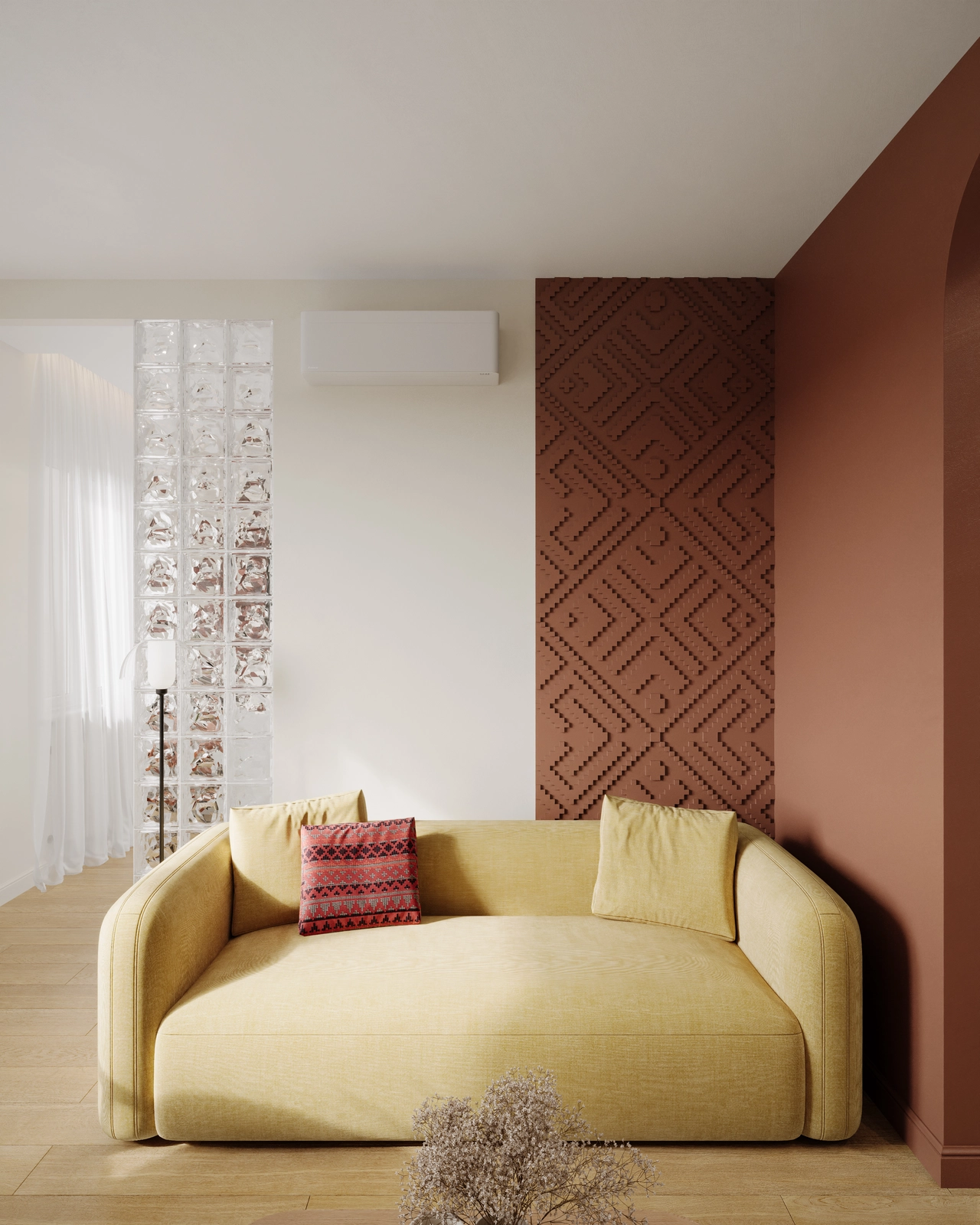 O canapea de culoare galben deschis, cu două perne decorative, se află în fața unui perete cu un model geometric maro, a unui perete despărțitor din blocuri de sticlă și a unei uși cu arc.