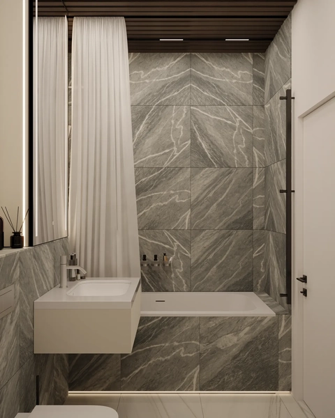 A modern bathroom featuring gray marble walls, a minimalist white sink with a wall-mounted faucet, and a glass shower partition. The space is brightened by soft lighting and has sheer white curtains hanging beside the shower area.