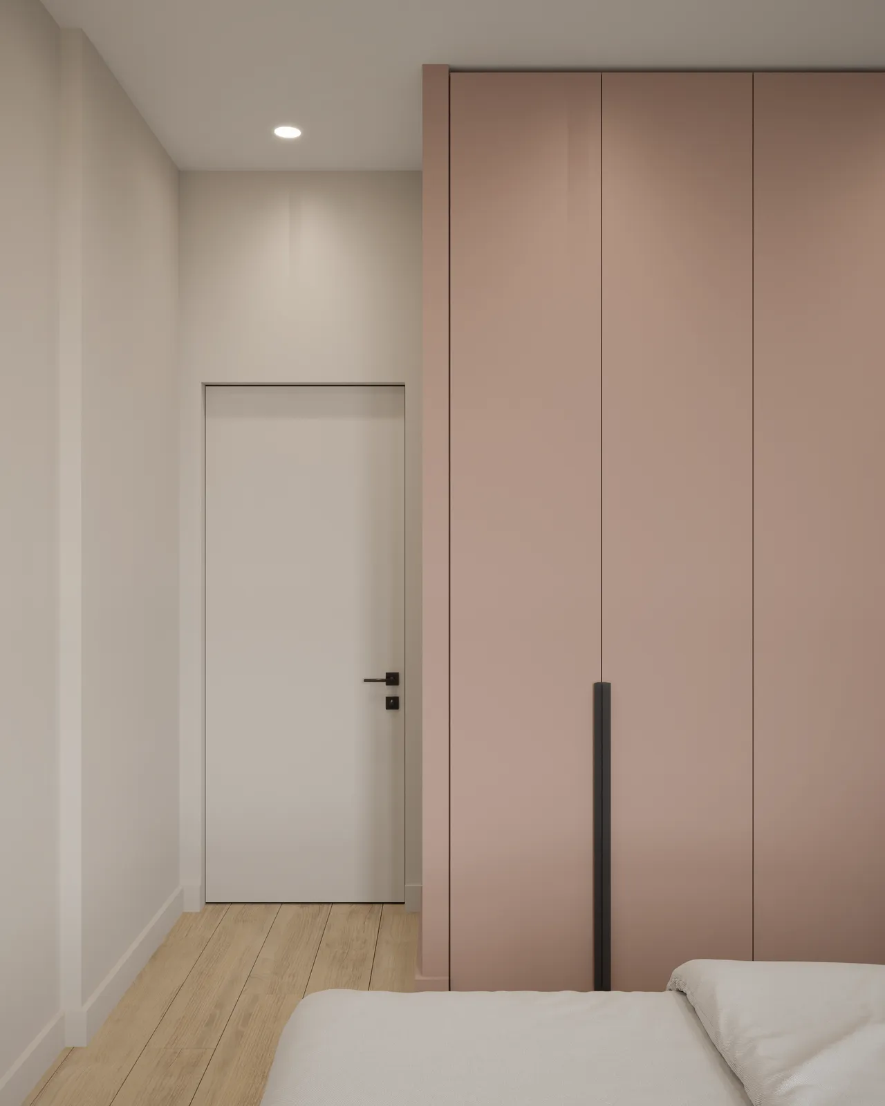 Minimalist bedroom interior featuring light wood floors, a white door, and a tall, blush pink built-in wardrobe with black handles, viewed from the foot of a white bed.