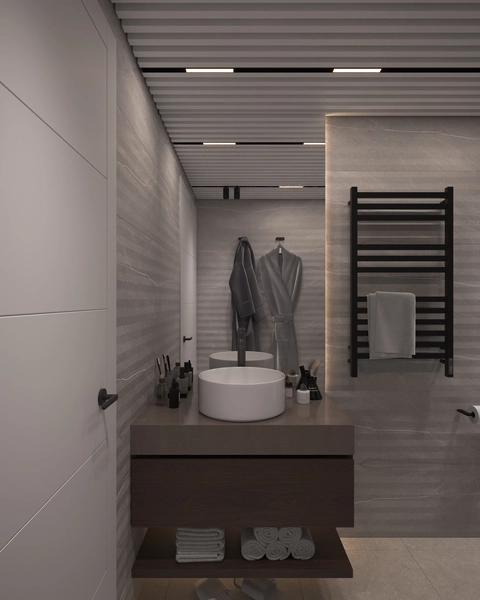 A bathroom in grey tones, with a round white washbasin on a stone countertop, wall-hung dark wood furniture, a black towel radiator and a slatted ceiling.
