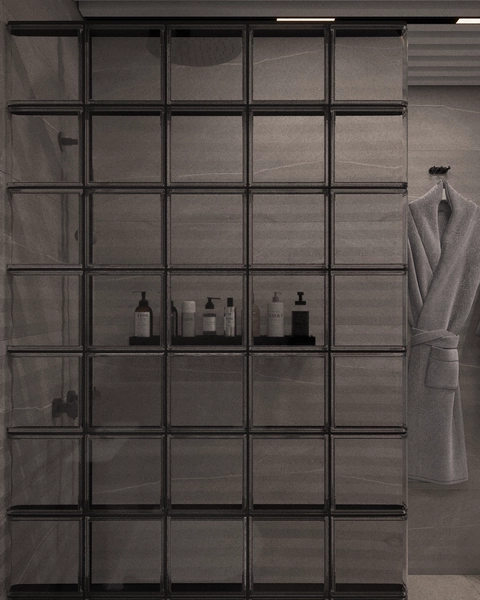 A detail of the shower area, with a partition of glass blocks with black profiles, a black shelf with cosmetic products and a bathrobe hanging on the wall.