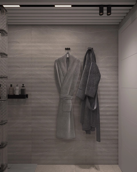A wall of grey stone-effect tiles, with two bathrobes hanging on black hooks, a wall-mounted shelf with bottles and linear lighting in the slatted ceiling.