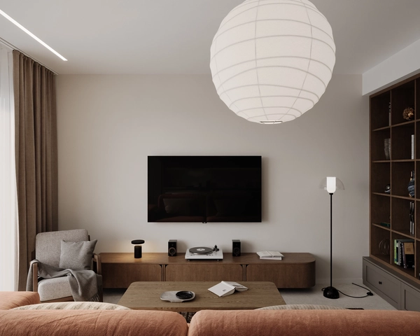 The TV area of the living room, with a television mounted on the wall, a long wooden console with a record player and speakers, a white spherical pendant lamp and the terracotta sofa in the foreground.