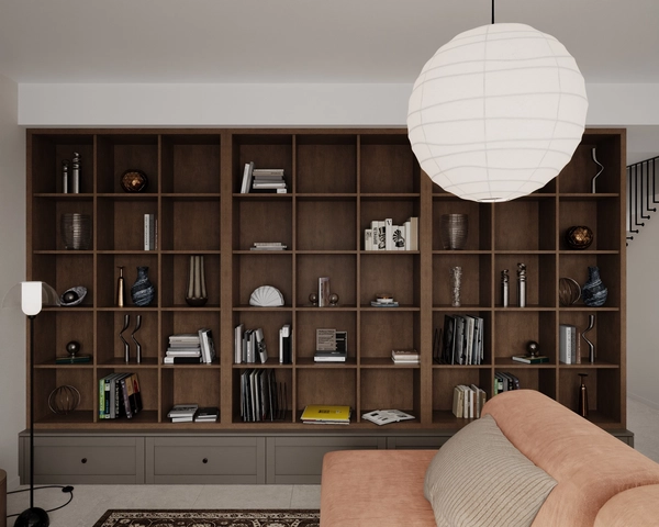 The full-wall bookcase of the living room, made of dark wood, with open niches for books and decorative objects and closed lower units, lit by a white spherical pendant lamp.
