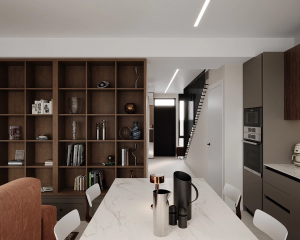 The dining area with a white marble countertop, white chairs and metal accessories, with a view towards the entrance hall and the staircase with its black railing, next to the column of built-in ovens.