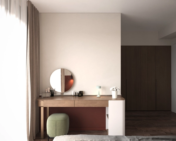 The light wood dressing table, with a round mirror, a table lamp and a green upholstered pouf, placed next to the beige drapes and the dark wood wardrobe.