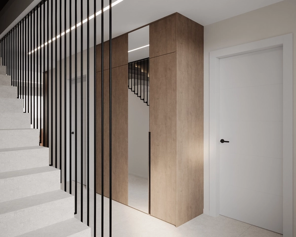 The entrance area, with a tall oak wardrobe with a mirror insert, a white door with a black handle and the staircase with its railing of vertical metal rods.