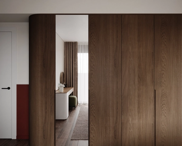 A detail of the walnut wardrobe with a rounded corner and a mirror panel reflecting the dressing table, the drapes and the wooden floor.