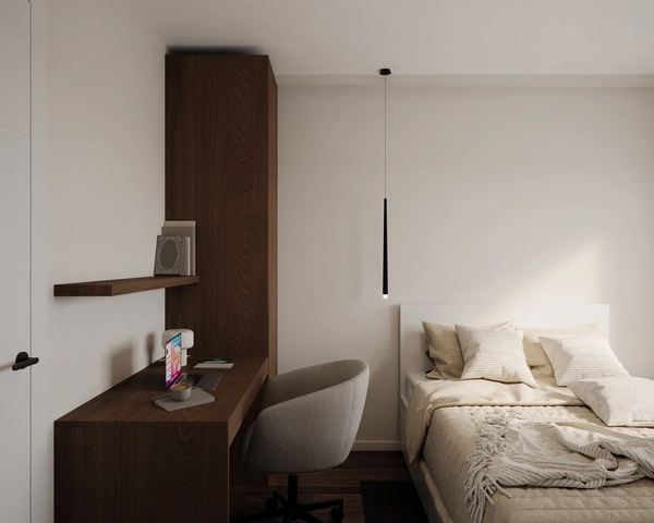 A minimalist bedroom, with a built-in dark wood desk, a wall-mounted shelf, a grey upholstered chair, a black linear pendant lamp and a bed with cream linen.